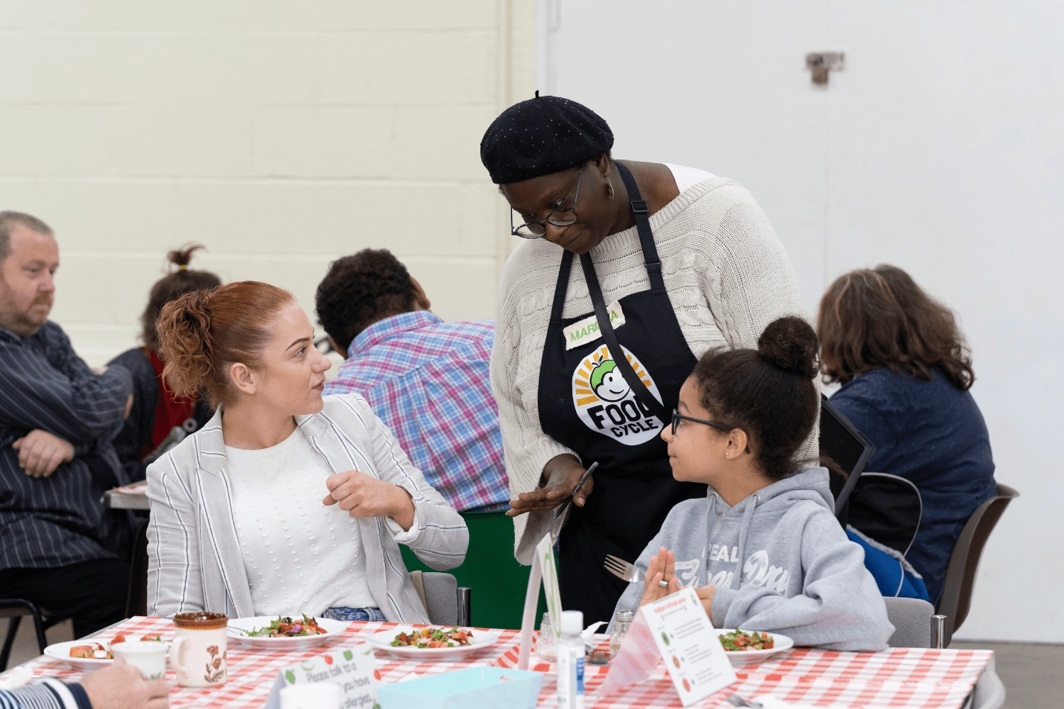 Child and Adult eating a community meal with volunteer speaking to them.