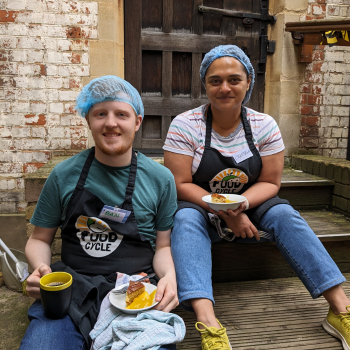 Volunteers, Chandana and Dan, sat holding food at a FoodCycle volunteering session.